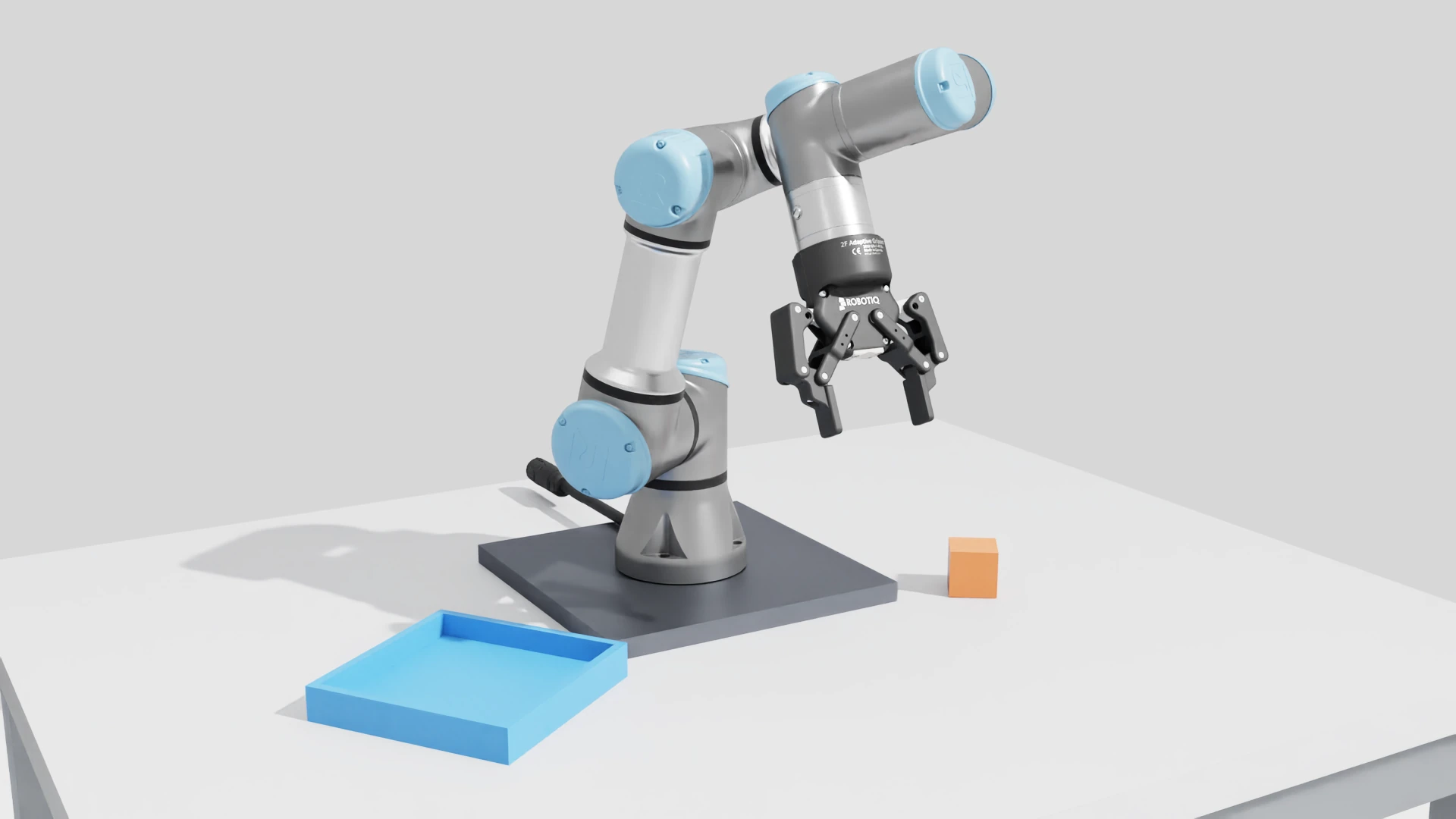 UR3e robot with blue joint covers and a Robotiq gripper above a worktable, orange cube and blue receiving tray.